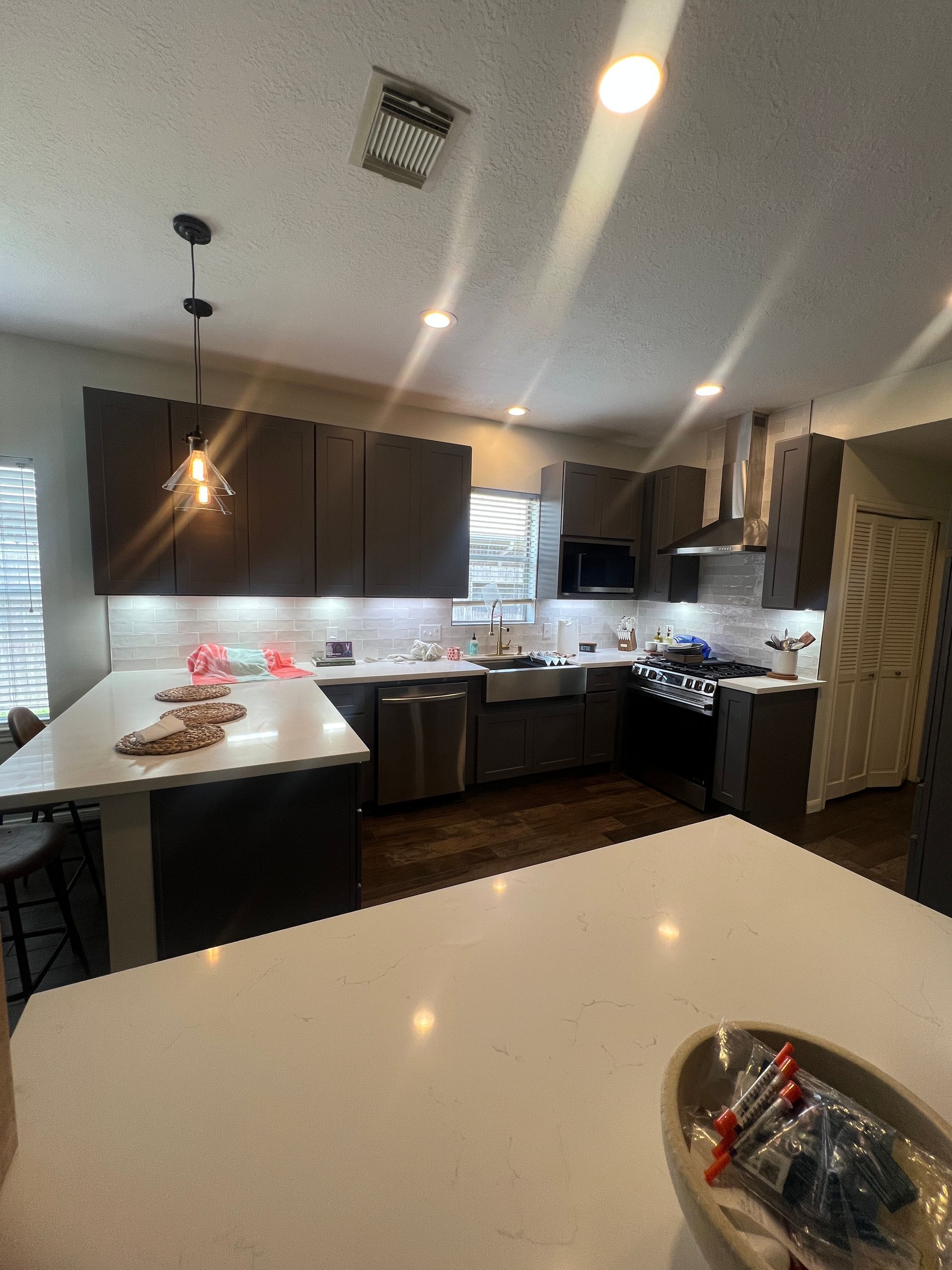Modern kitchen with dark cabinets, white countertops, stainless steel appliances, and dark wood floors.