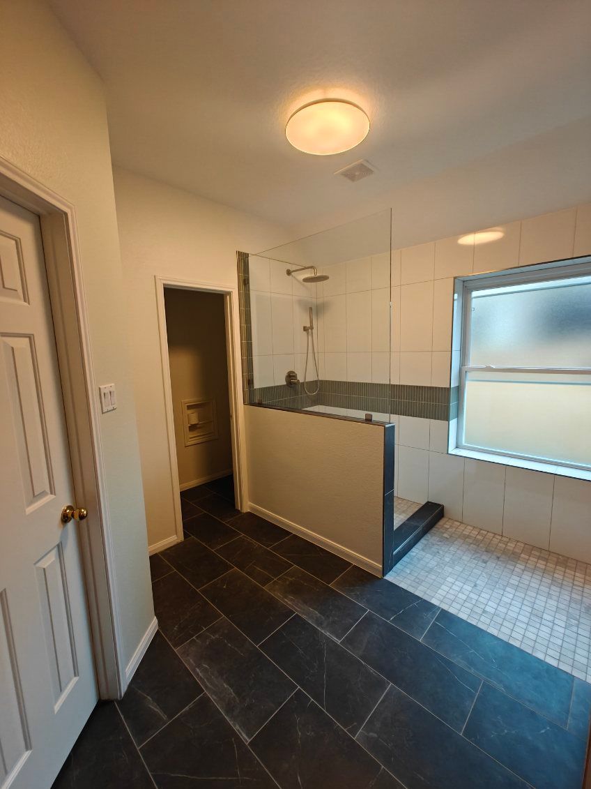 Bathroom with dark tiled floor, shower, white walls, and a door.