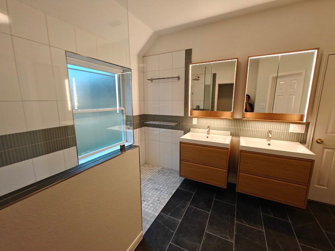 A modern bathroom with two wooden vanities, large mirrors, and a tiled shower.