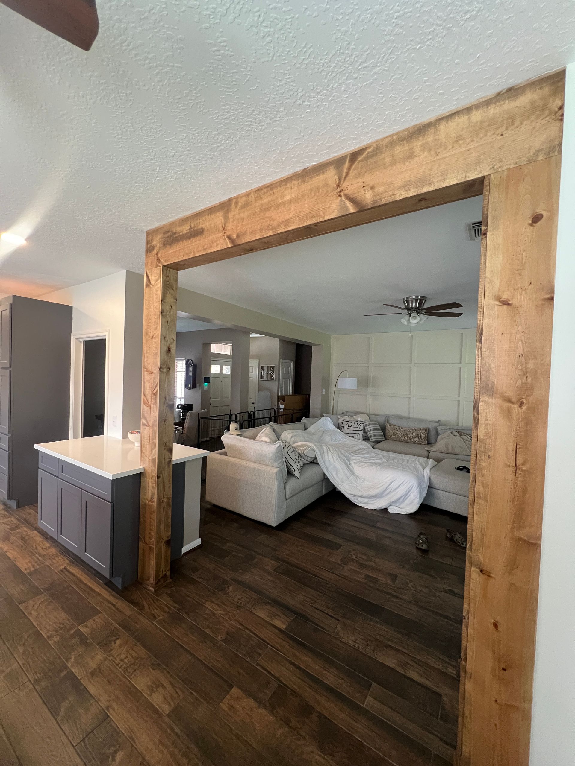 Wooden doorway frame in a home with a living room visible. Dark flooring, gray cabinets.