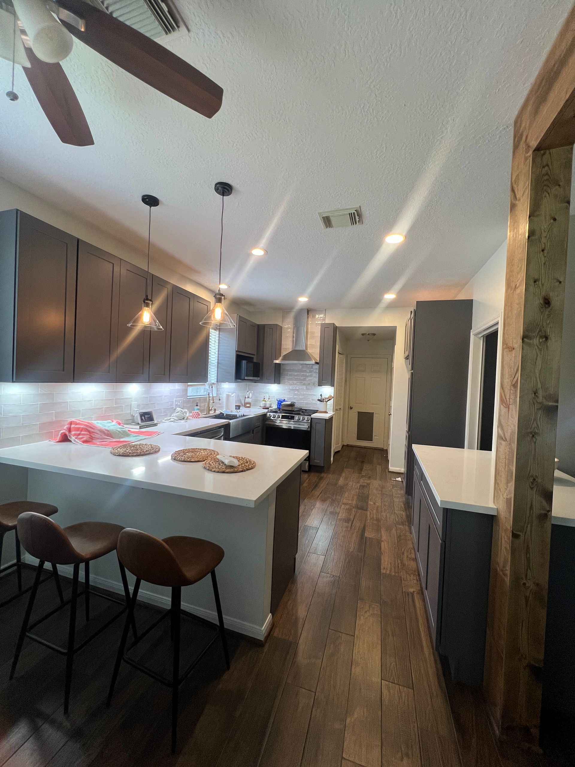 Modern kitchen with dark gray cabinets, white countertops, and brown wood floors.