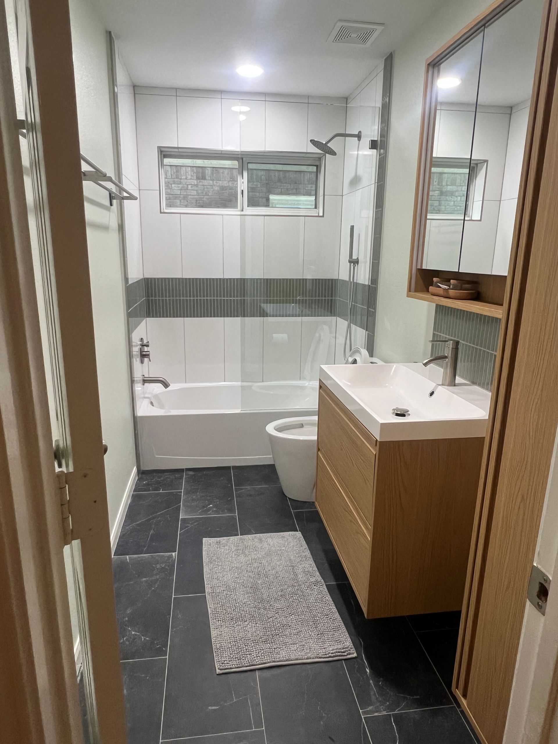 Modern bathroom with a tub, vanity, and dark tile floor.