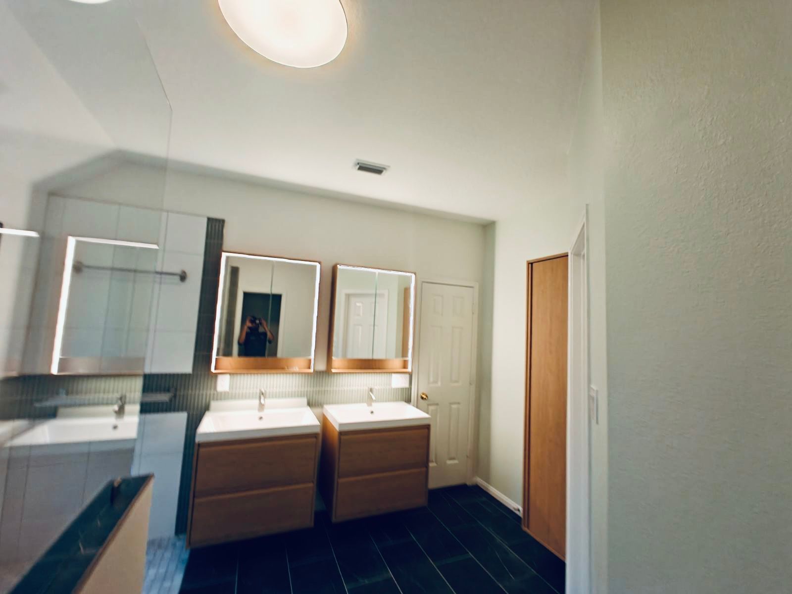 Bathroom with two sinks, wood vanities, and white cabinets.  Black tiled floor and white walls.