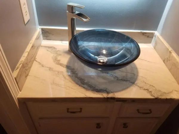 Vanity with vessel sink; blue glass bowl sink on white marble counter, modern faucet, white cabinet.