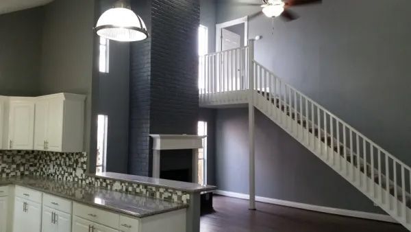 Kitchen and stairs; white cabinets, granite countertops, gray walls, fireplace, and a loft.