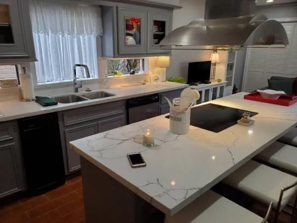 Gray and white kitchen with island and sink, black appliances, wood floors.