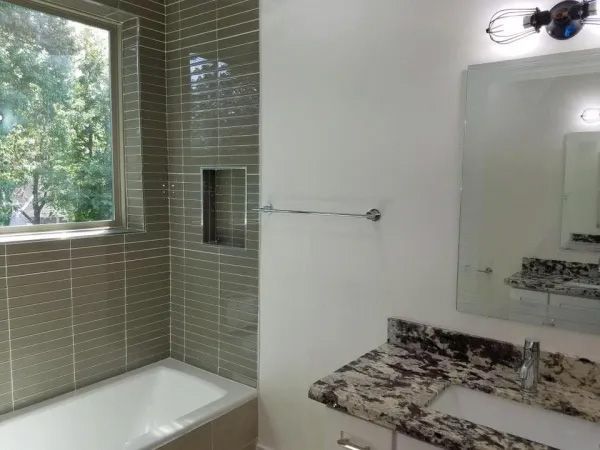 Bathroom with tub, tiled walls, granite countertop, window with outside view.