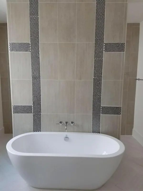 Freestanding white bathtub in a beige tiled bathroom with decorative mosaic tile accents.