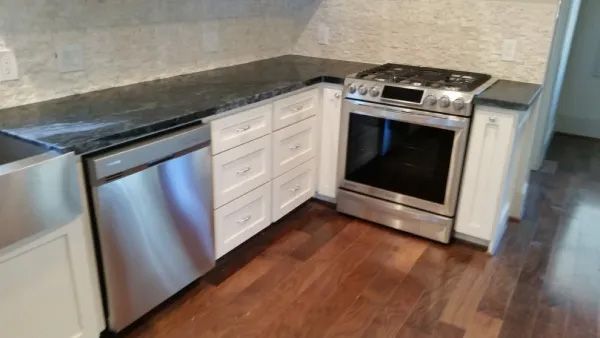 Stainless steel appliances in a kitchen with white cabinets, dark countertops, and wood floors.