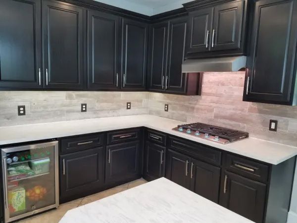 Black kitchen cabinets with white countertops and tiled backsplash; stainless steel appliances.