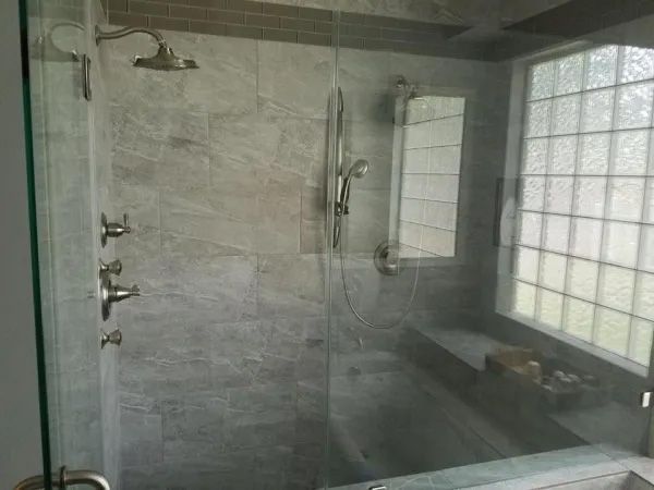 Modern shower with glass doors, gray tile walls, and a built-in bench next to a frosted window.