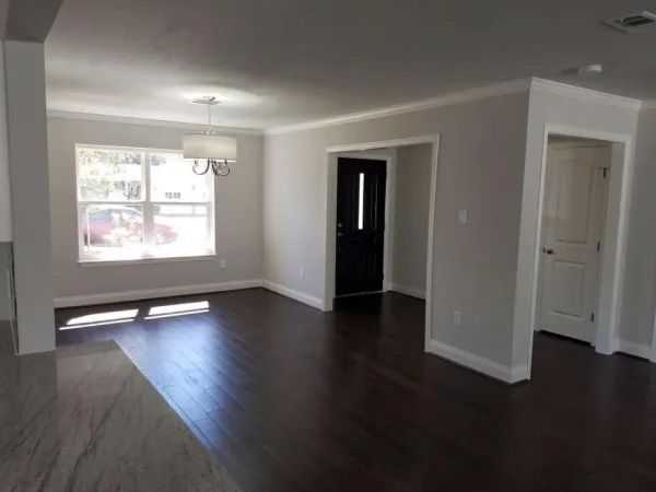 Empty living room with dark wood floors, gray walls, white trim, and a black front door.