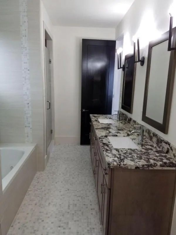 Bathroom with double vanity, black door, bathtub, and marble tile floor.