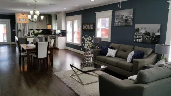 Open-concept living space: gray sofa, dark accent wall, dining area, kitchen, hardwood floors.