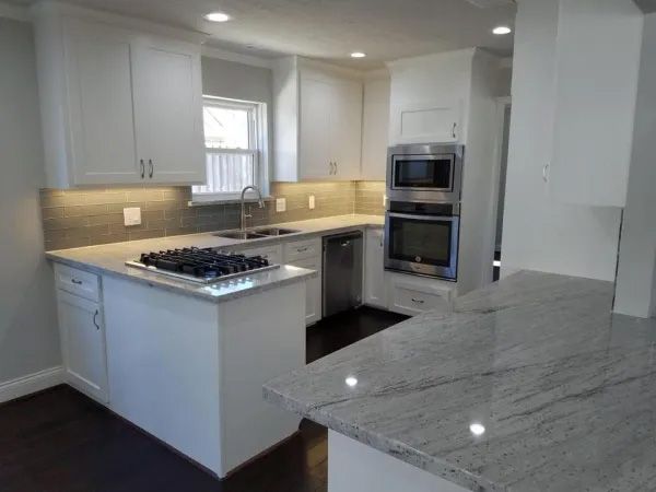 Modern white kitchen with granite countertops, stainless steel appliances, and dark wood floors.