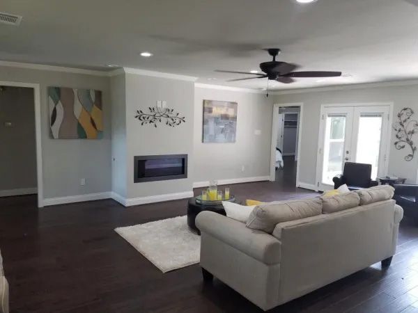 Spacious living room with dark wood floor, gray walls, fireplace, and a tan sofa; art on walls.