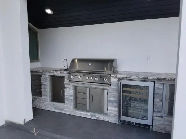 Outdoor kitchen with a stainless steel grill, sink, and wine cooler on a gray stone countertop.