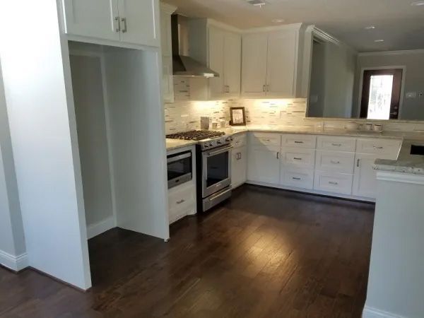 White kitchen with dark wood floors, stainless steel appliances, and overhead cabinets.