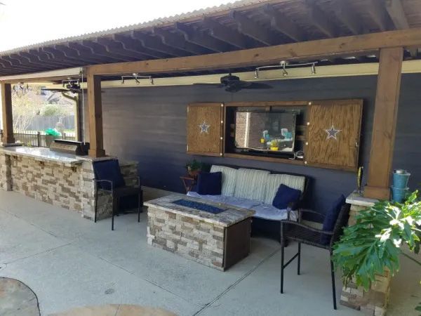 Outdoor patio with built-in bar, seating, fireplace, and TV in wooden cabinet with star accents.