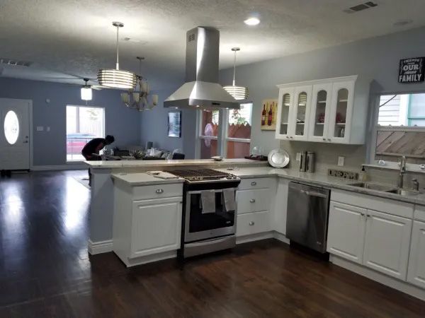 Bright kitchen with white cabinets, stainless steel appliances, and dark wood floors.