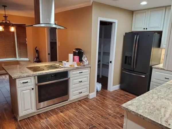 Kitchen with island, stove, oven, white cabinets, stainless steel appliances, and wood floor.