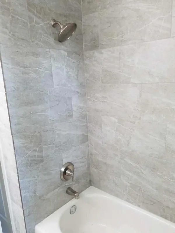 Shower with gray marble-patterned tile, white tub, and silver fixtures.
