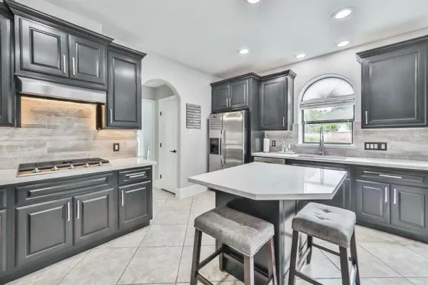 Kitchen with dark gray cabinets, white countertops, and a central island with two stools.
