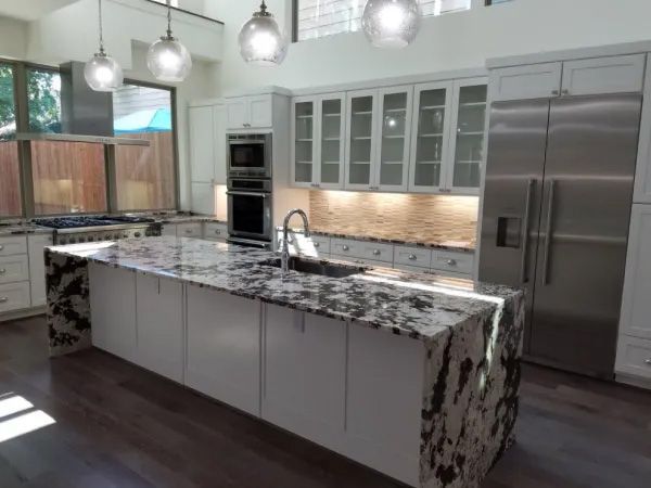 Modern kitchen with a large island, white cabinets, stainless steel appliances, and dark granite countertops.