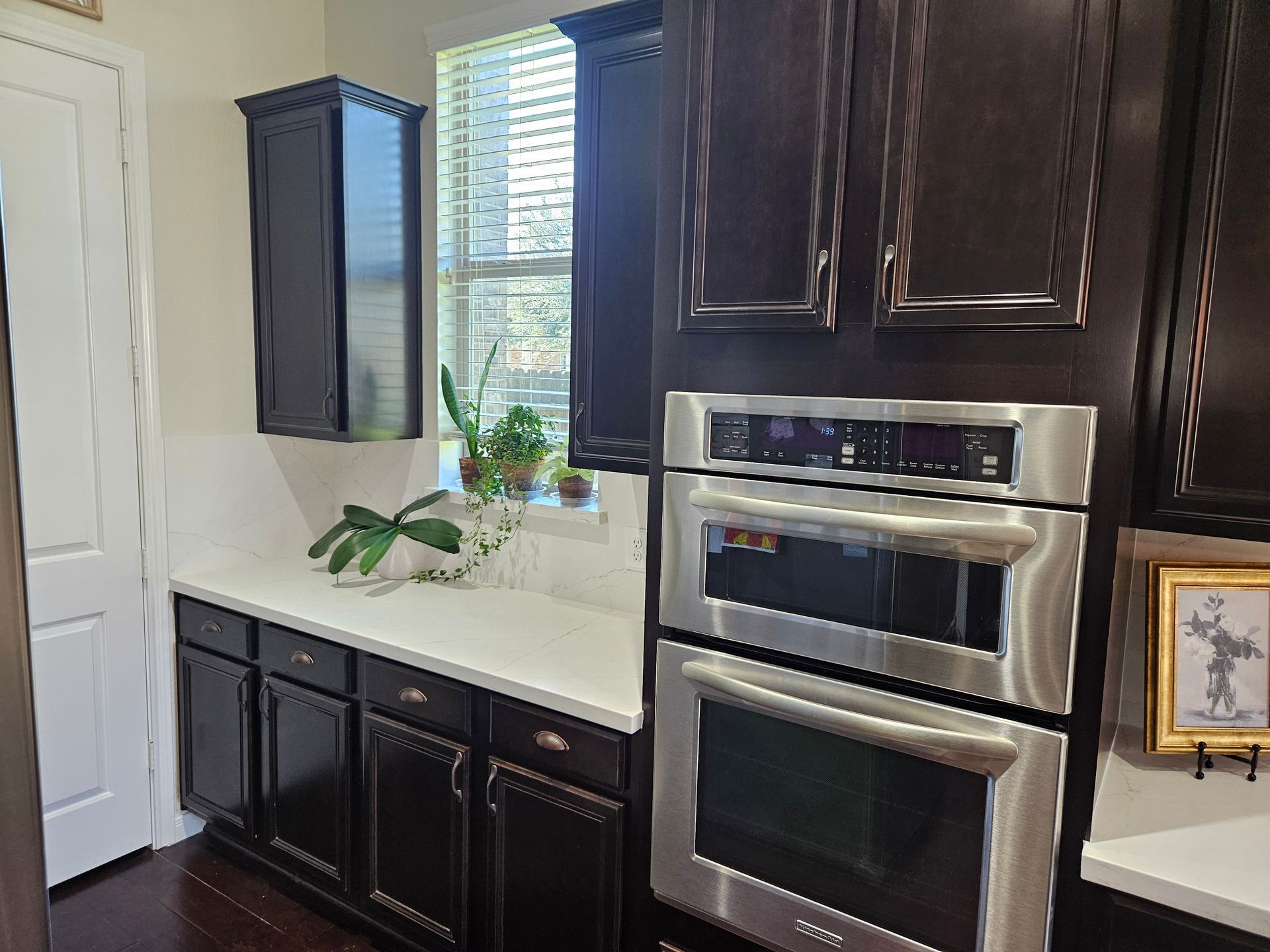 Dark wood kitchen with white countertop, stainless steel oven, and window with plants.
