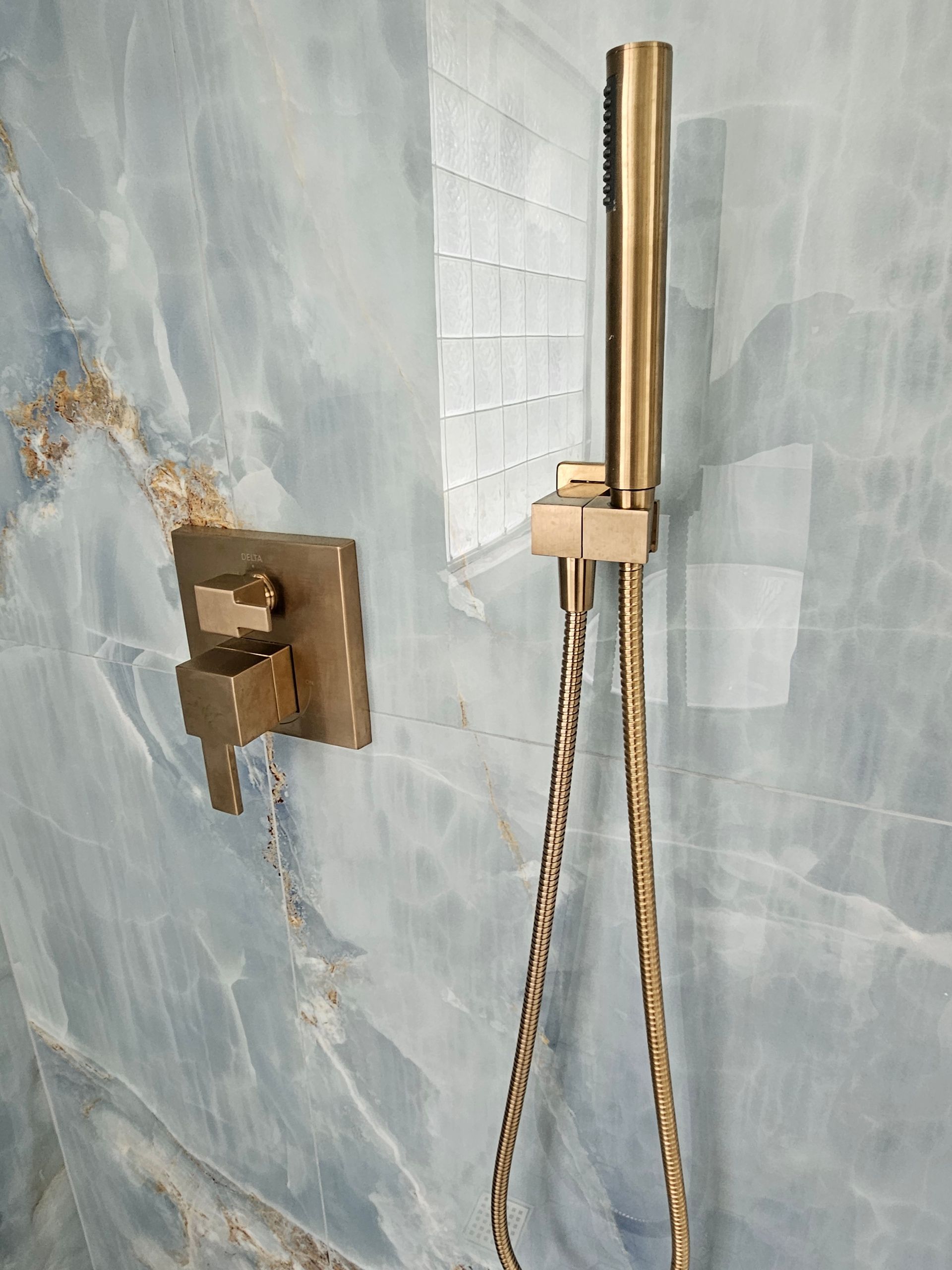 Gold shower fixtures against a blue marble wall, with a tiled accent.