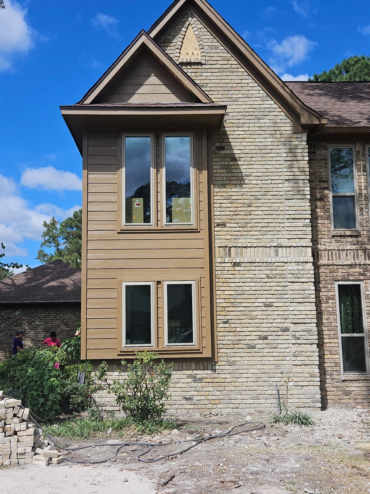 Two-story house with brick facade, a wooden bay window, and brown roof against a blue sky.