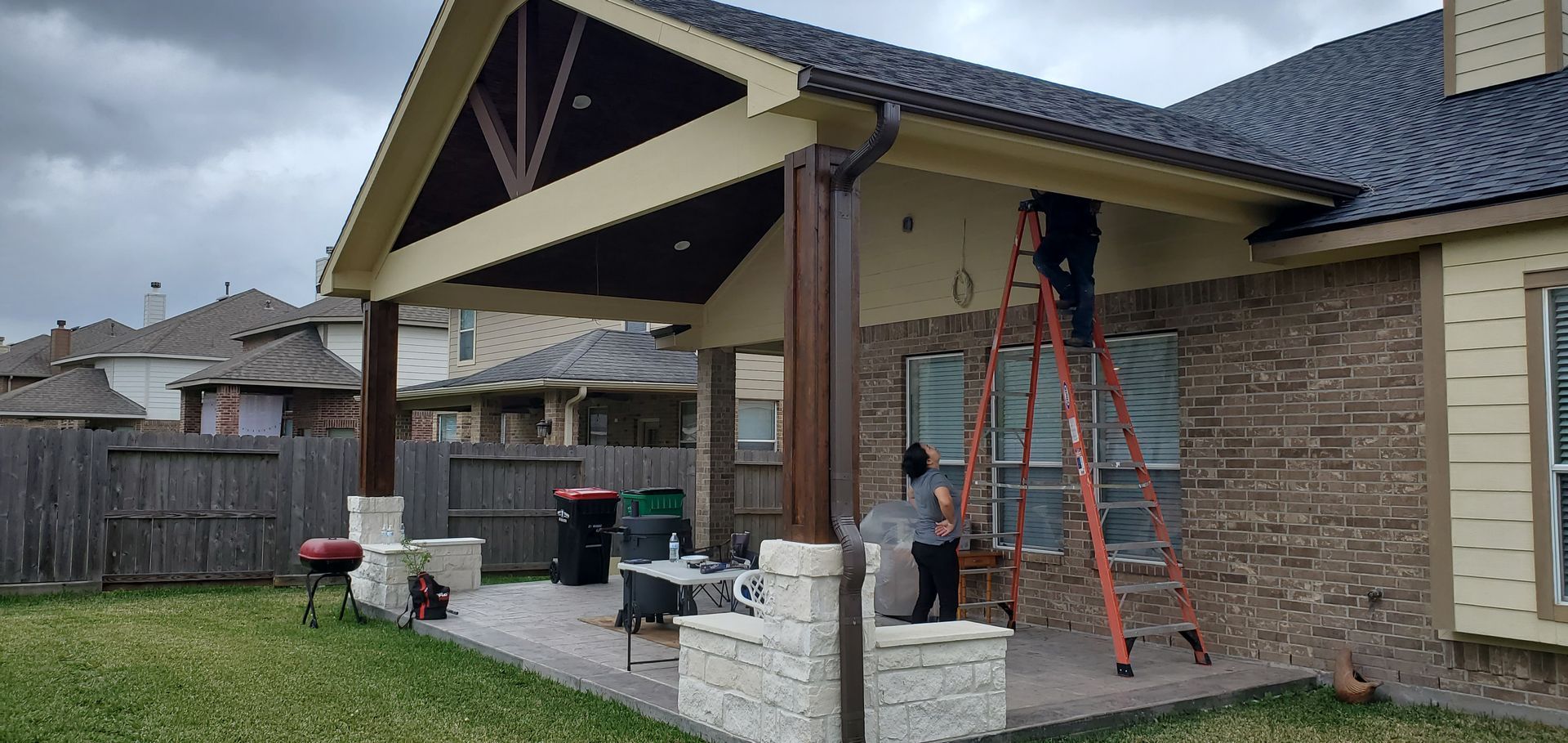 Two people on a ladder are working on a house with a patio.