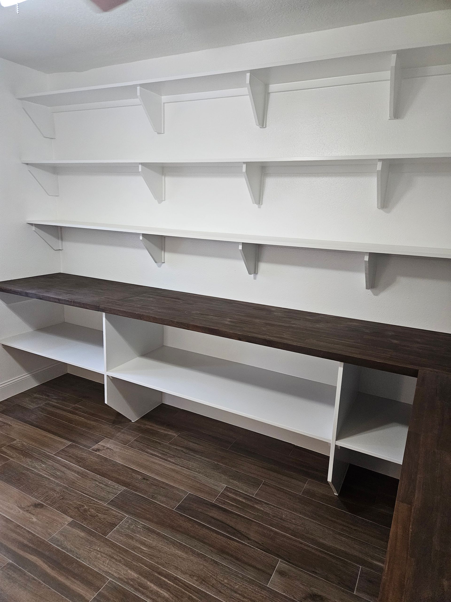 Built-in pantry with white shelves and a dark countertop, on wood-look flooring.