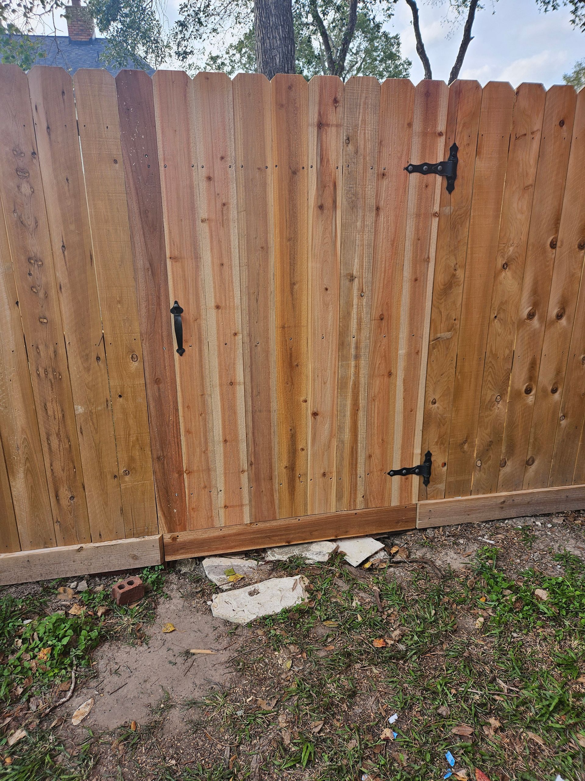 Wooden fence with gate, brown wood, black hinges and latch, set outdoors.