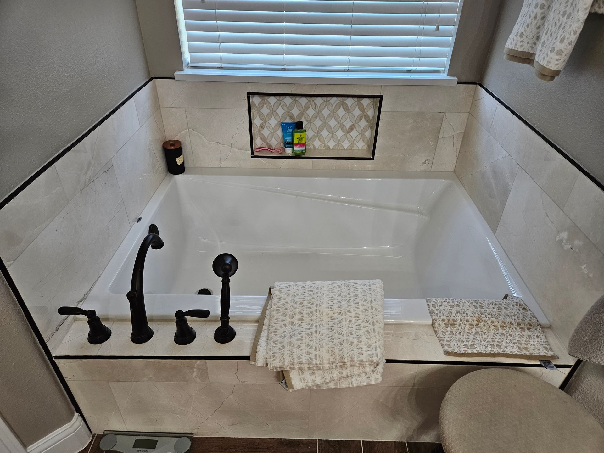 Bathroom with white bathtub, black fixtures, tile surround, window above.