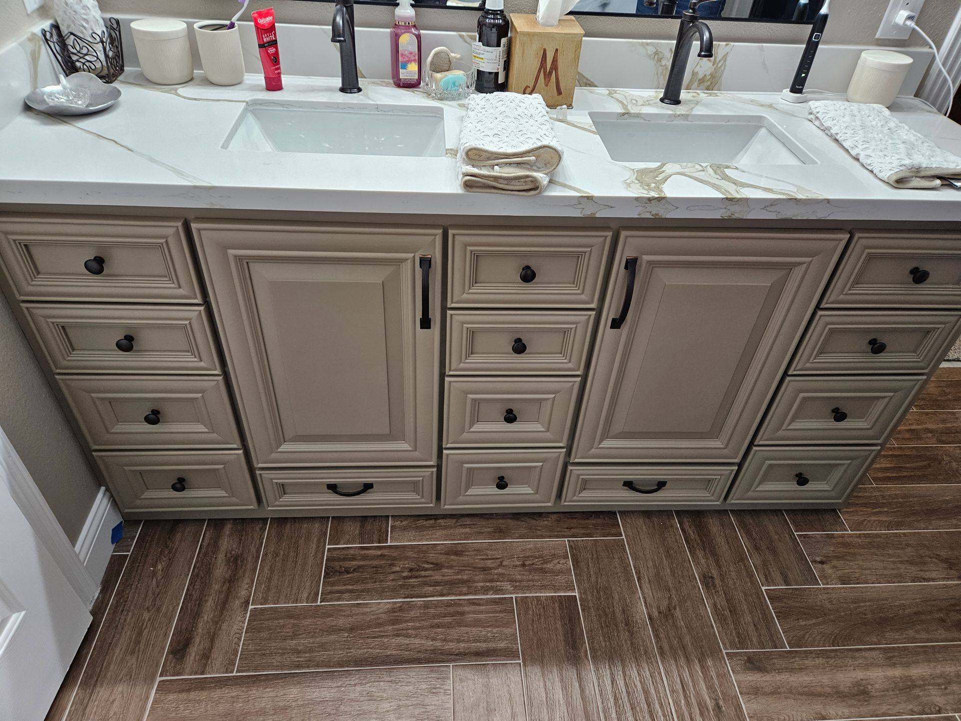 Beige double vanity with black hardware, two sinks, and wood-look floor tiles.