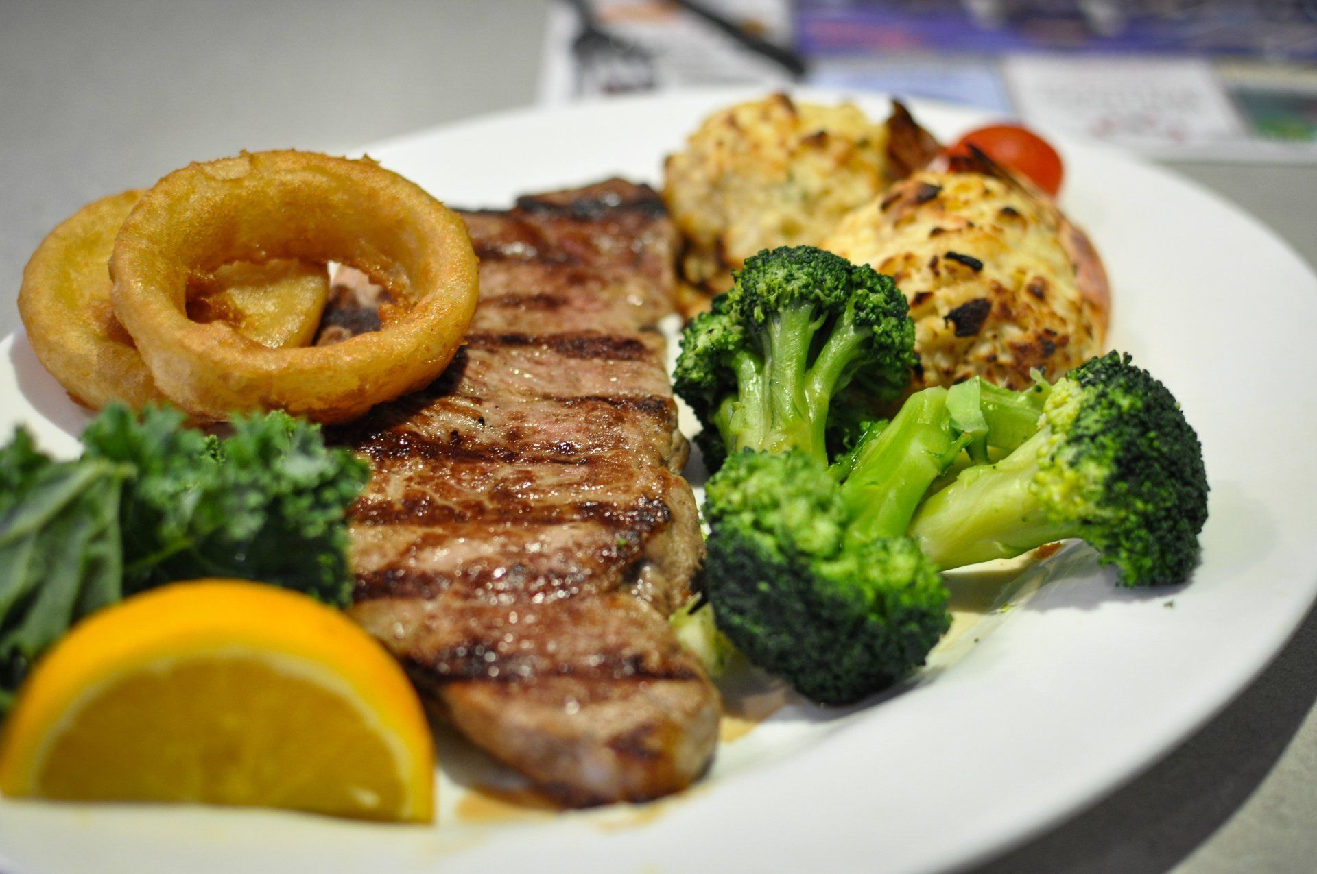 A white plate topped with a steak , broccoli and onion rings.