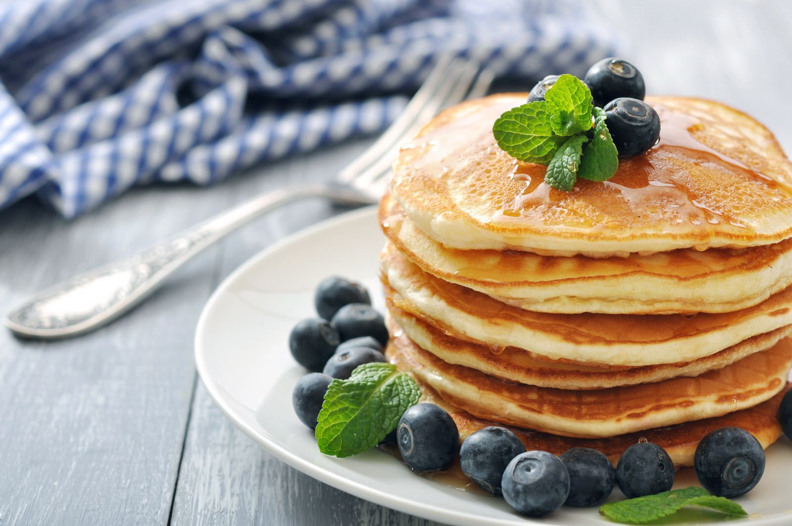 A stack of pancakes with blueberries and mint on a white plate.