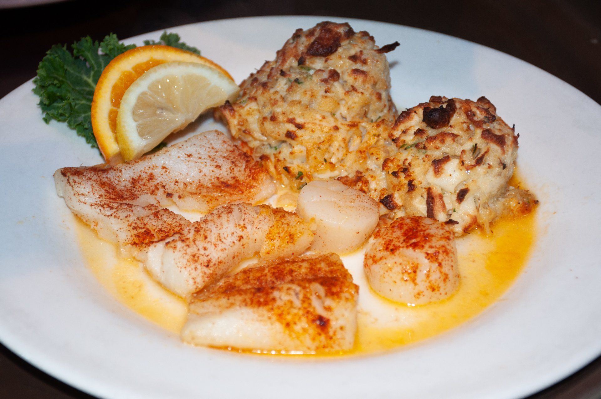 A white plate topped with fish , scallops and crab cakes.