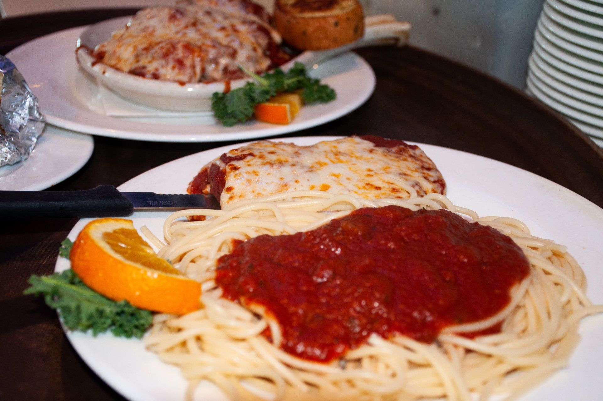 A plate of spaghetti with sauce and an orange slice on a table.