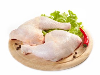 Muslos de pollo crudos sobre una tabla de cortar de madera con lechuga y pimientos.