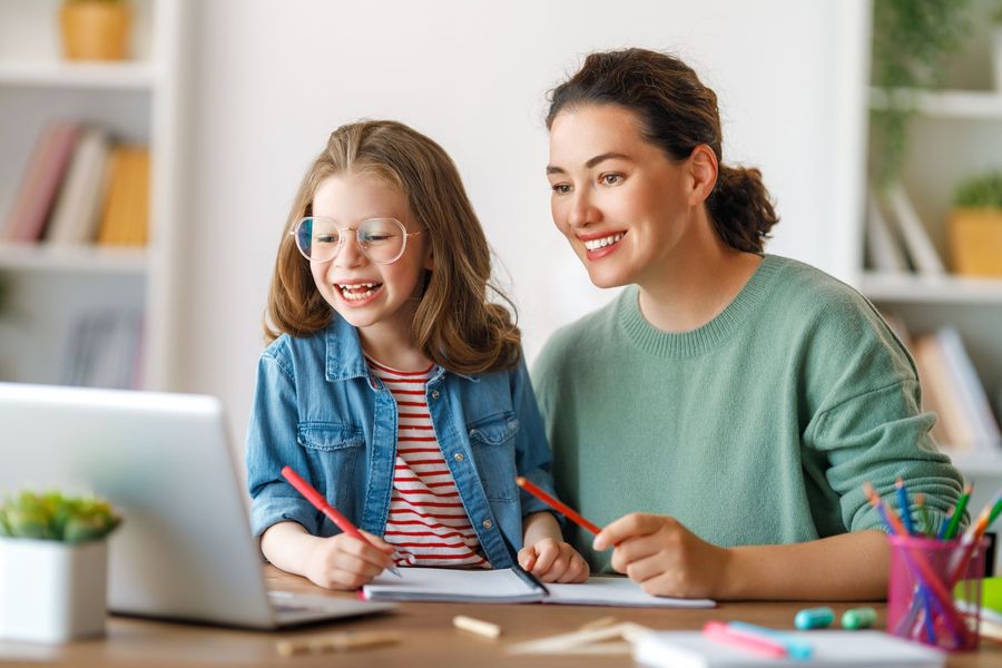 A woman and a little girl are sitting at a table looking at a laptop.