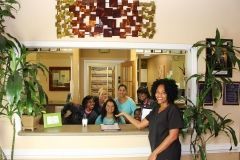 A woman is standing in front of a reception desk with a group of people behind her.