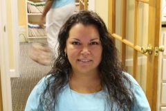 A woman in a blue shirt is sitting in front of a door and smiling.