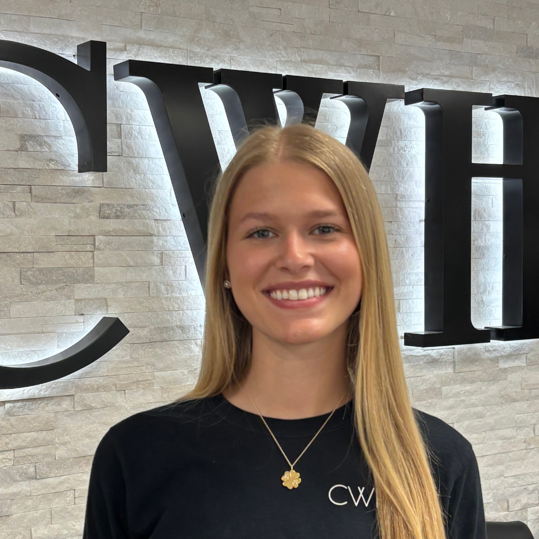 Smiling woman in a black shirt standing before a lit CWH sign on a stone wall