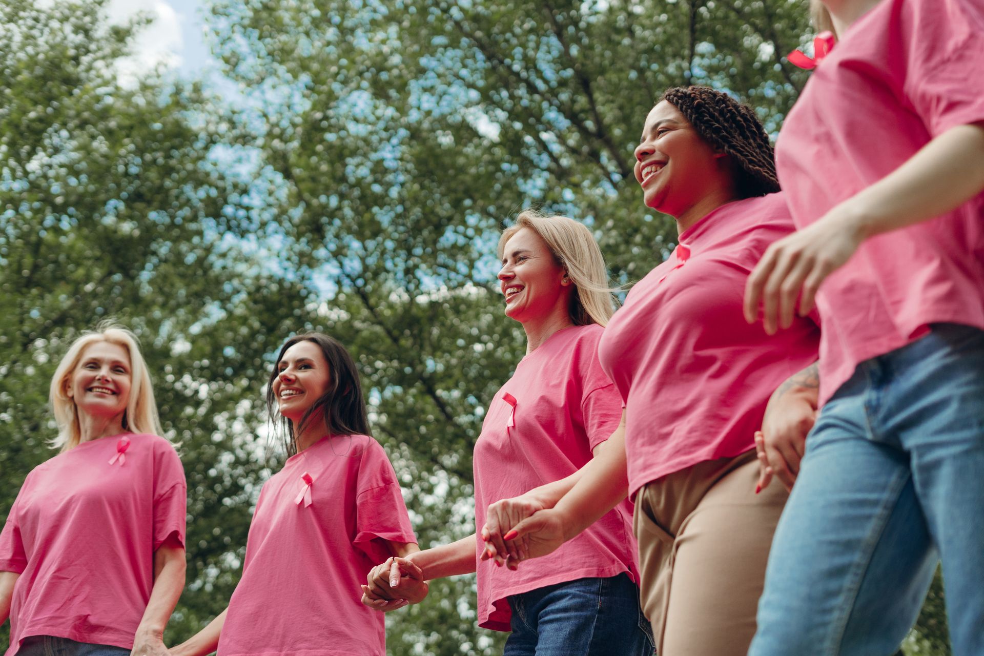 People in pink shirts walking outdoors in a park, smiling and holding hands