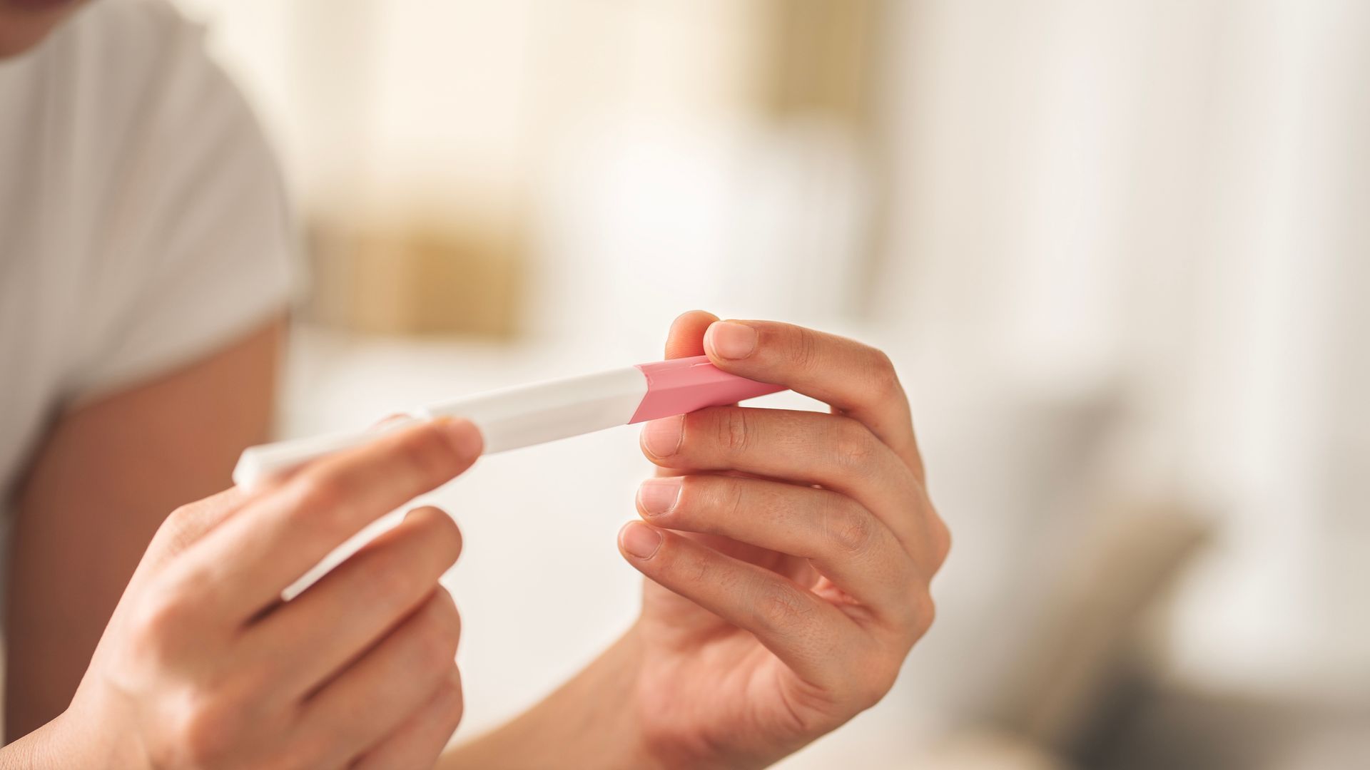 Hands holding a pregnancy test with a pink cap in a softly lit room