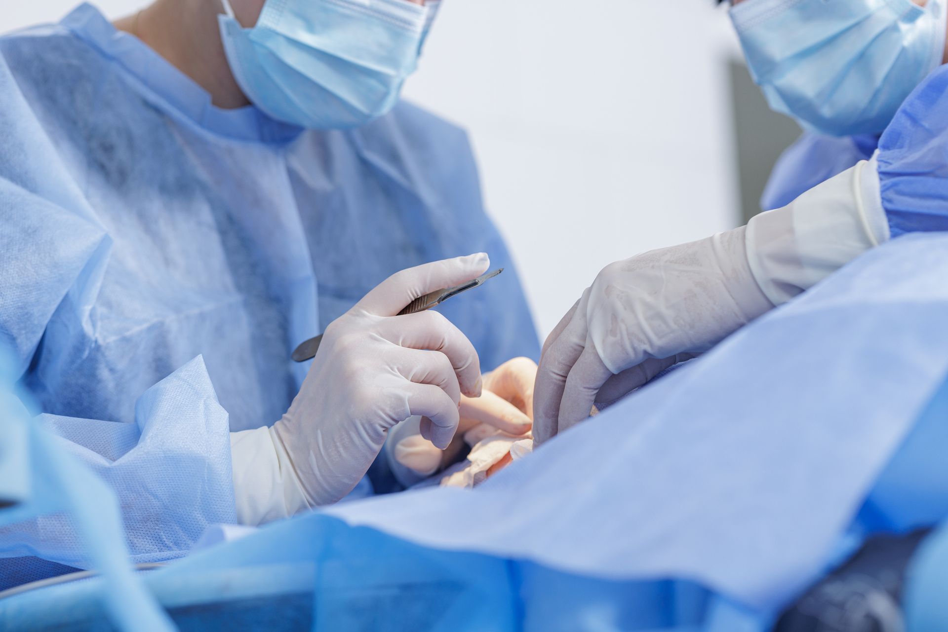 Surgeons in blue scrubs and gloves perform an operation in an operating room