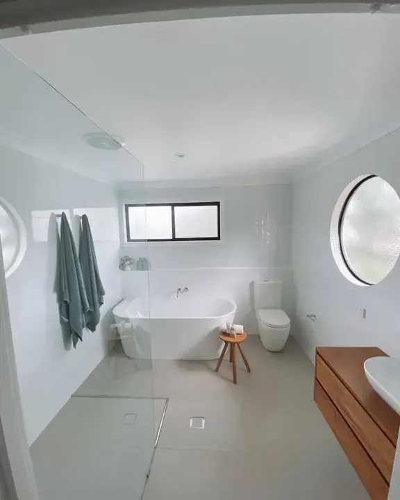 A Bathroom with A Toilet, Basket, and Towels Hanging on The Wall — Aqua Blue Plumbing Services in Coffs Harbour, NSW