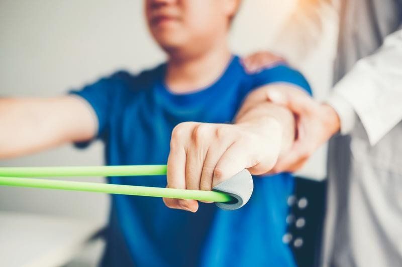 A young boy is being helped by a doctor with a resistance band.